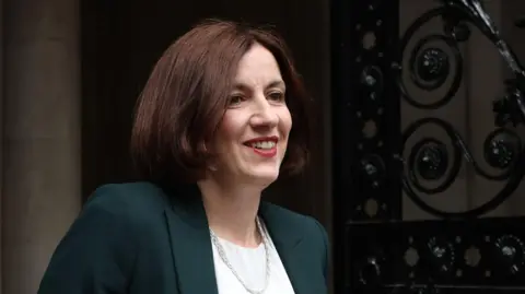 EPA Bridget Phillipson smiles as she arrives for the first meeting of the Cabinet of the new Labour government in Downing Street. She has short brown hair, is wearing a dark green jacket, a white blouse and has a silver necklace.