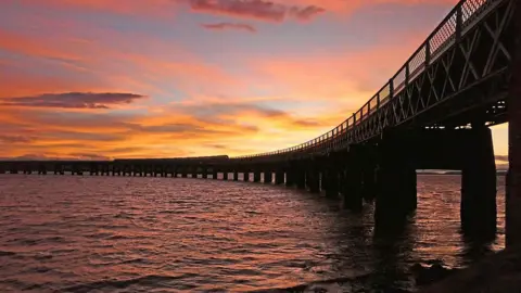 BBC Weather Watchers/Wellies Full of Water A large pier with a sunset behind