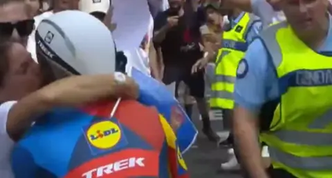 Eurosport Cyclist Julien Bernard kissing his wife who has come onto the road, he is pictured from behind and other spectators are crowding the road