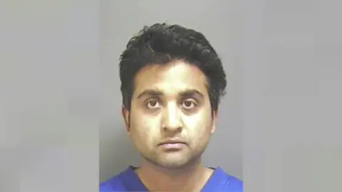 Devon and Cornwall Police Police mugshot of Salil Korambayil, who has black hair and is wearing a blue t-shirt