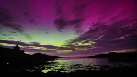 PA Media Aurora borealis in Howick, Northumberland, showing the sky in layers of purple, indigo and various shades of green, with hilly terrain and river below in silhouette
