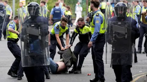 Man on the ground with coat pulled up over his head is grabbed by Irish police officers