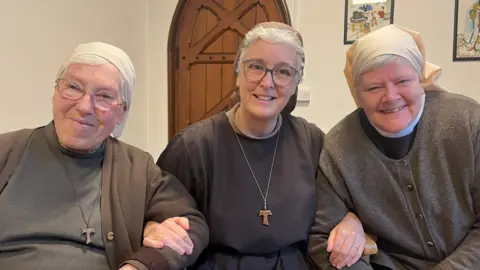 The Poor Clares of Arundel: Sisters Aelred, Gabriel and Leo, sat together linking arms, dressed in their nun's habits