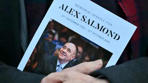 Order of Service for the memorial service to Alex Salmond, with a photo of him in a suit.