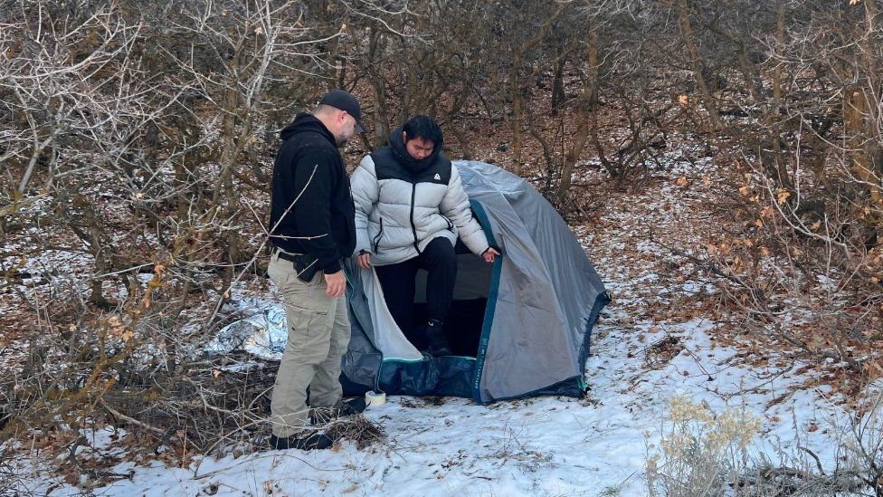 Kai Zhuang climbs out of a tent as an officer looks on