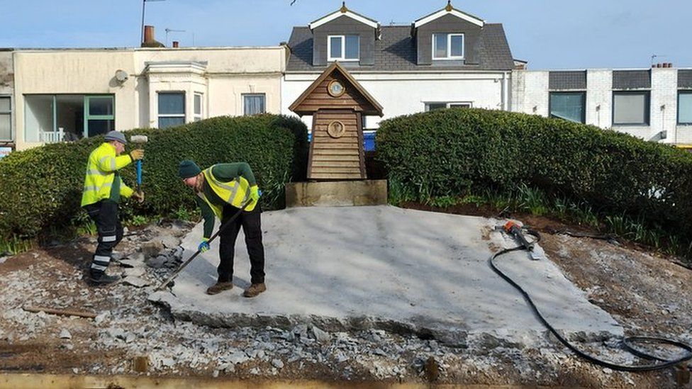 Two workmen removing the concrete covering beside the flower clock