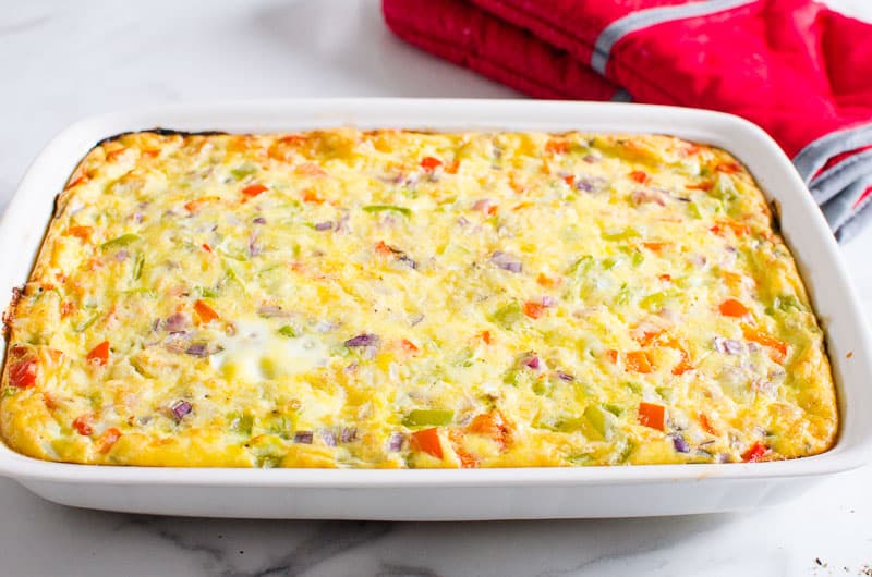 Healthy breakfast egg bake in white baking dish and red oven mitts nearby.