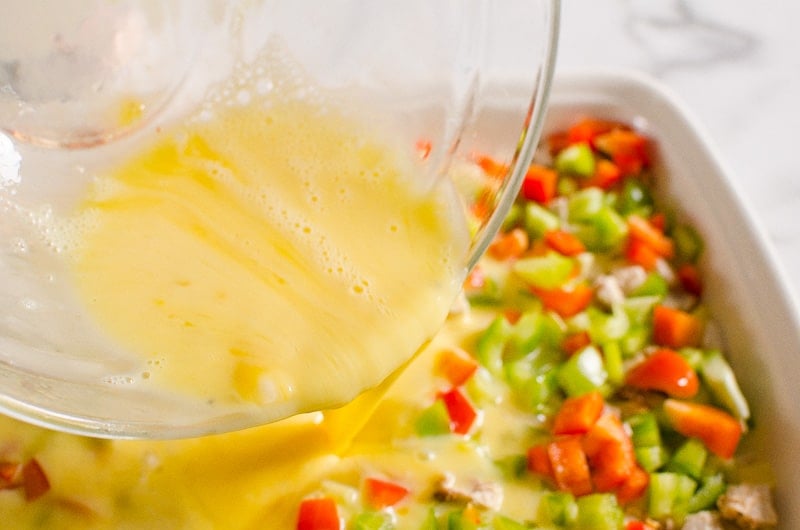 Pouring egg mixture over chopped veggies and meat.