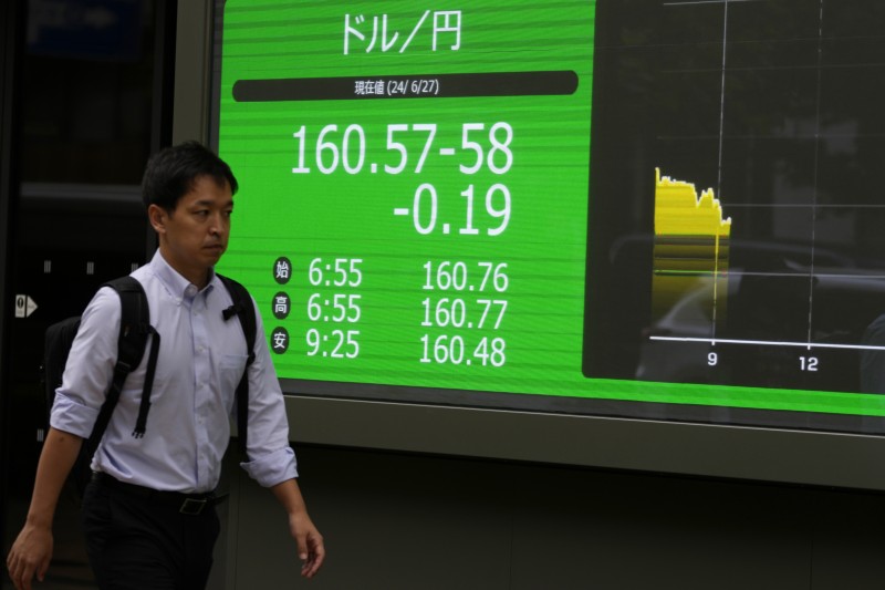 2024年6月27日。東京一家證券公司外一個人走過顯示美元和日圓匯率的電子股票板。（美聯社）