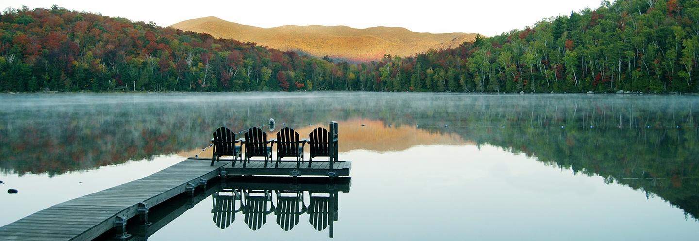 Adirondack chairs at the end of a dock facing the mountain view