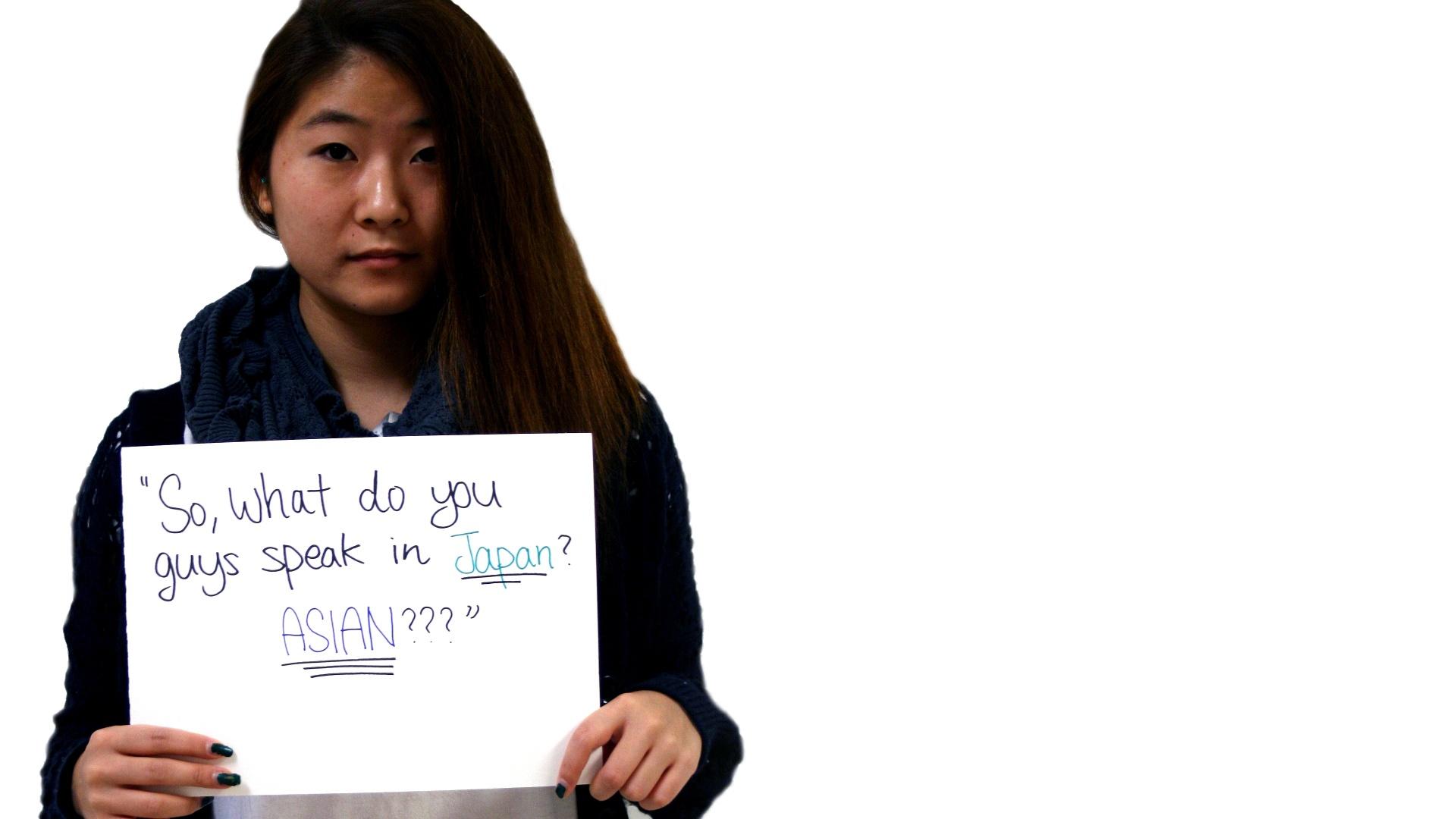 A young woman holds a sign of a question, depicting a microaggression.