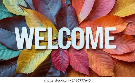 A welcome sign made of white letters on a background of colorful autumn leaves in various shades of red, orange, yellow, and green.