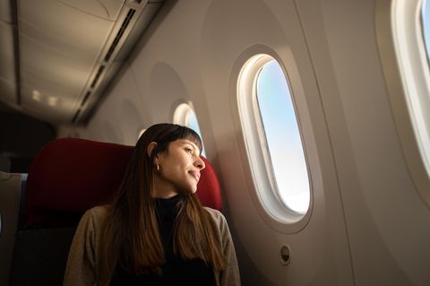 Tipps für Langstreckenflüge: Eine Frau zieht im Flugzeug und schaut aus dem Fenster.