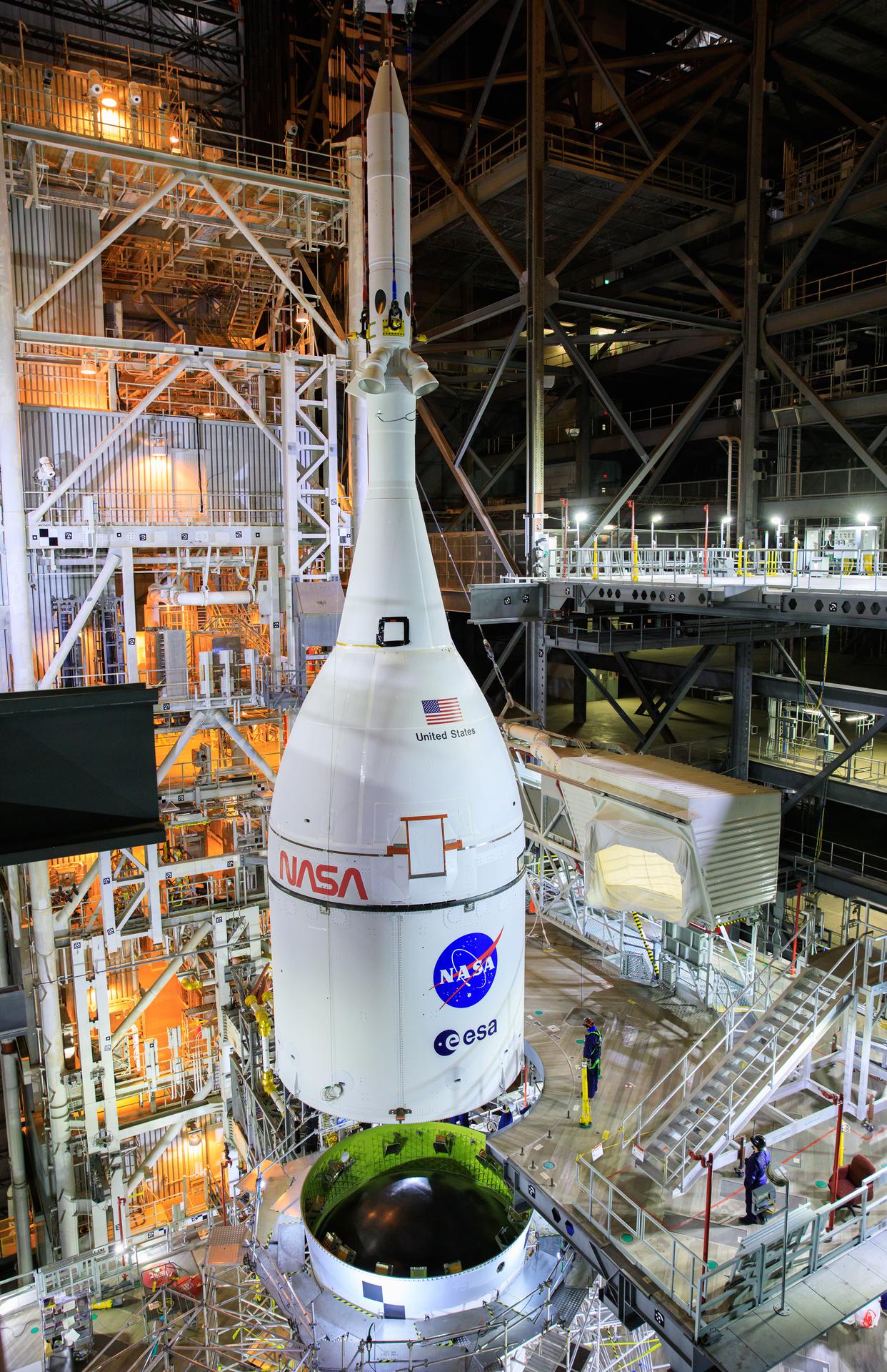 The Orion spacecraft for NASA’s Artemis I mission, fully assembled with its launch abort system, is lifted above the Space Launch System (SLS) rocket in High Bay 3 of the Vehicle Assembly Building at Kennedy Space Center in Florida on Oct. 20, 2021. The stacking of Orion on top of the SLS completes assembly for the Artemis I flight test. Teams will begin conducting a series of verification tests ahead of rolling out to Launch Complex 39B for the Wet Dress Rehearsal. Artemis I will be an uncrewed test flight of the Orion spacecraft and Space Launch System rocket as an integrated system ahead of crewed flights to the Moon. Under Artemis, NASA aims to land the first woman and first person of color on the Moon and establish sustainable lunar exploration.