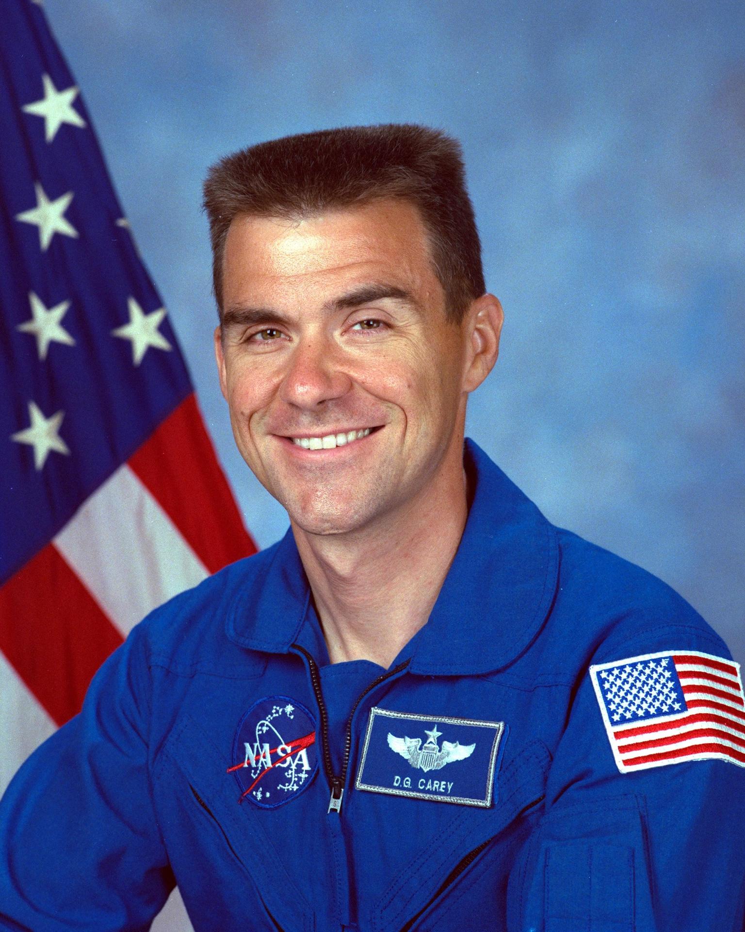 A man sits in front of the American flag and smiles