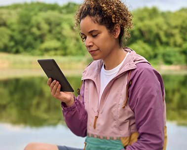 Eine Frau liest an einem See auf ihrem Kindle