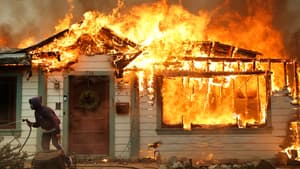 Une personne utilise un tuyau d'arrosage pour tenter de sauver une maison de l'incendie d'Eaton le 8 janvier 2025 à Altadena, en Californie.