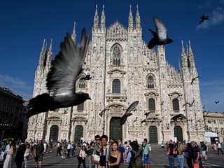 Des touristes posent pour une photo de famille alors que des pigeons passent devant la cathédrale Duomo à Milan, le 6 juillet 2023.