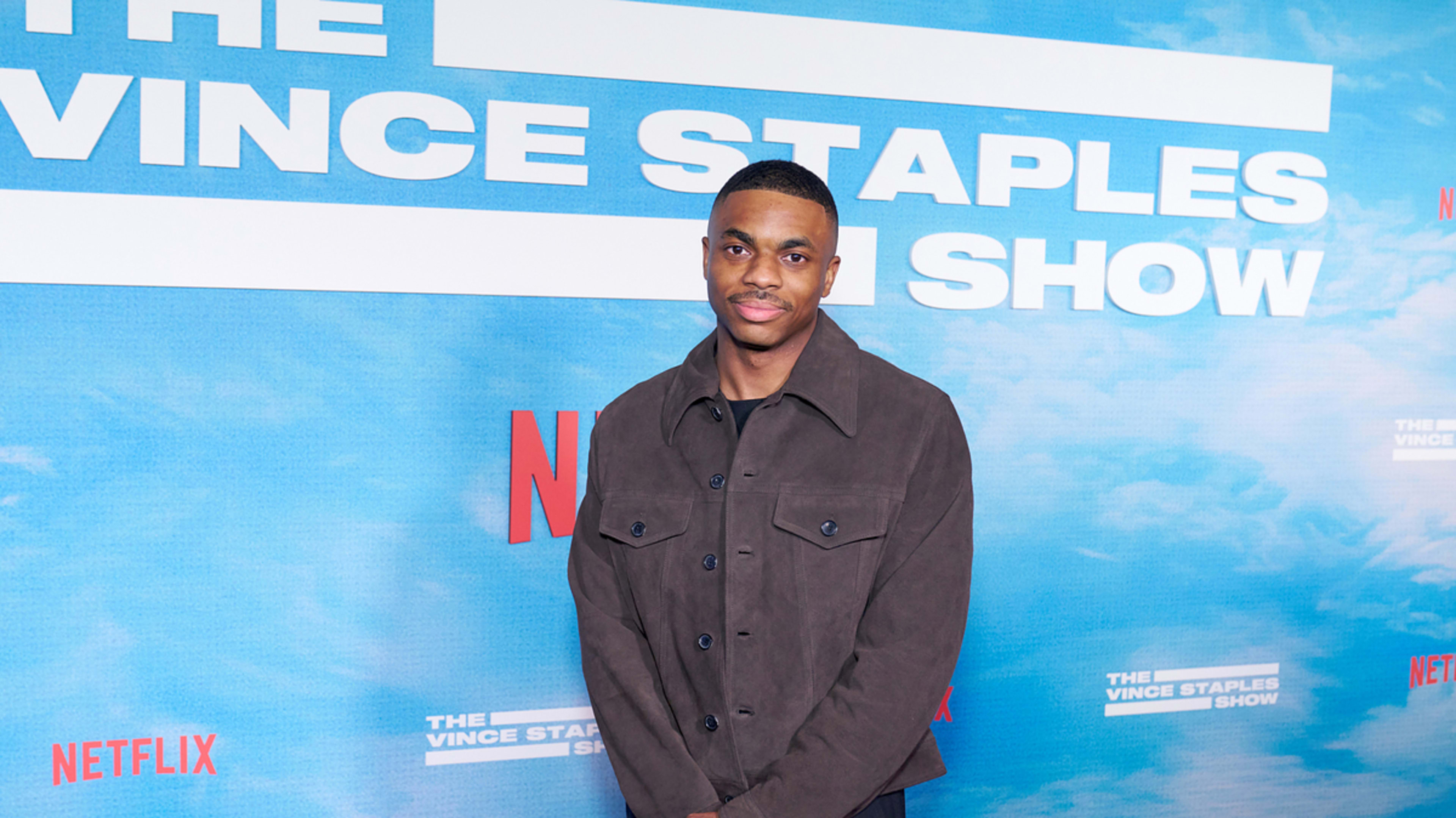 Man in dark casual jacket stands before a backdrop with text "The Vince Staples Show" and Netflix logos