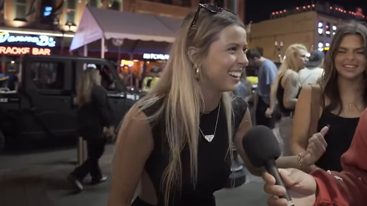 Two women laughing and interacting with a person holding a microphone on a lively street at night