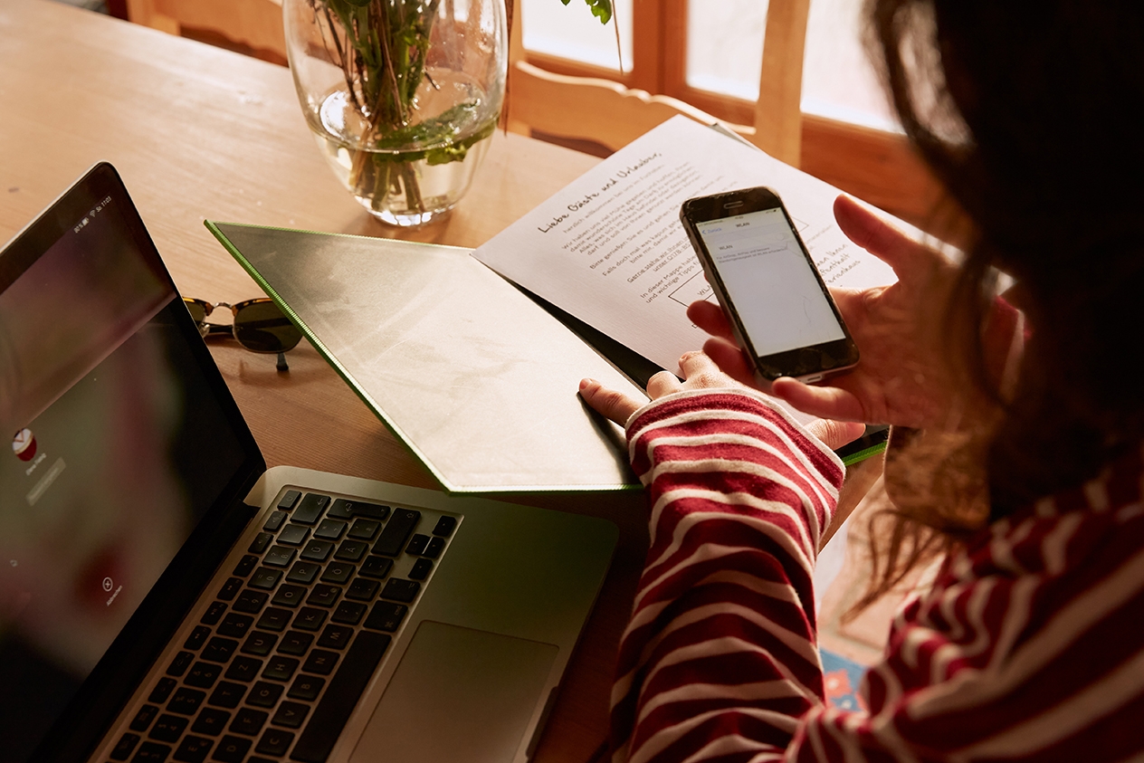 Une personne vérifie des informations sur son ordinateur et son téléphone portable tout en consultant des documents imprimés.