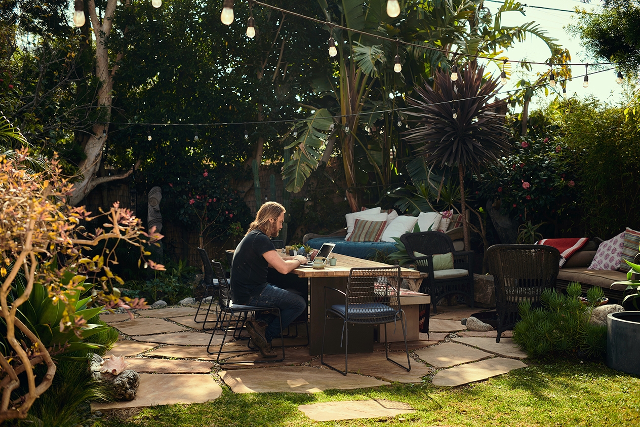 A person outside sitting a table, typing on their laptop.