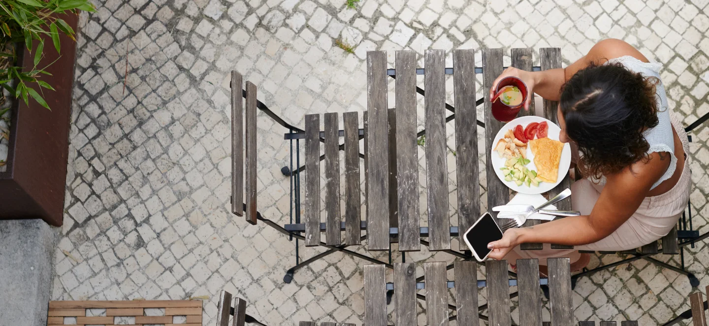 person sitting down at a table eating a meal while browsing their phone