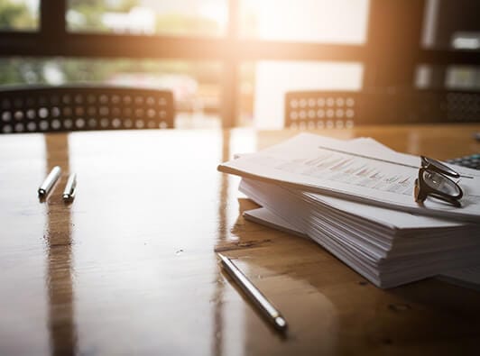 Lawyer's desk with pile of documents, scattered pens, and a pair of glasses