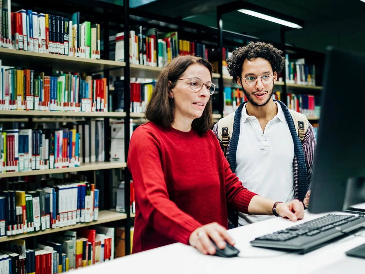 Librarian looking up books on computer for student