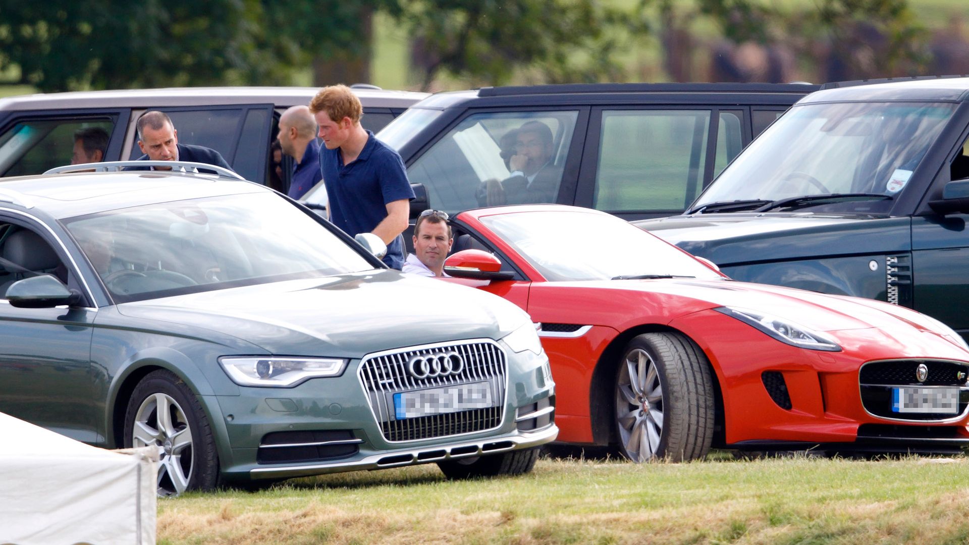 Peter Phillips in a red Jaguar with Prince Harry looking at a car