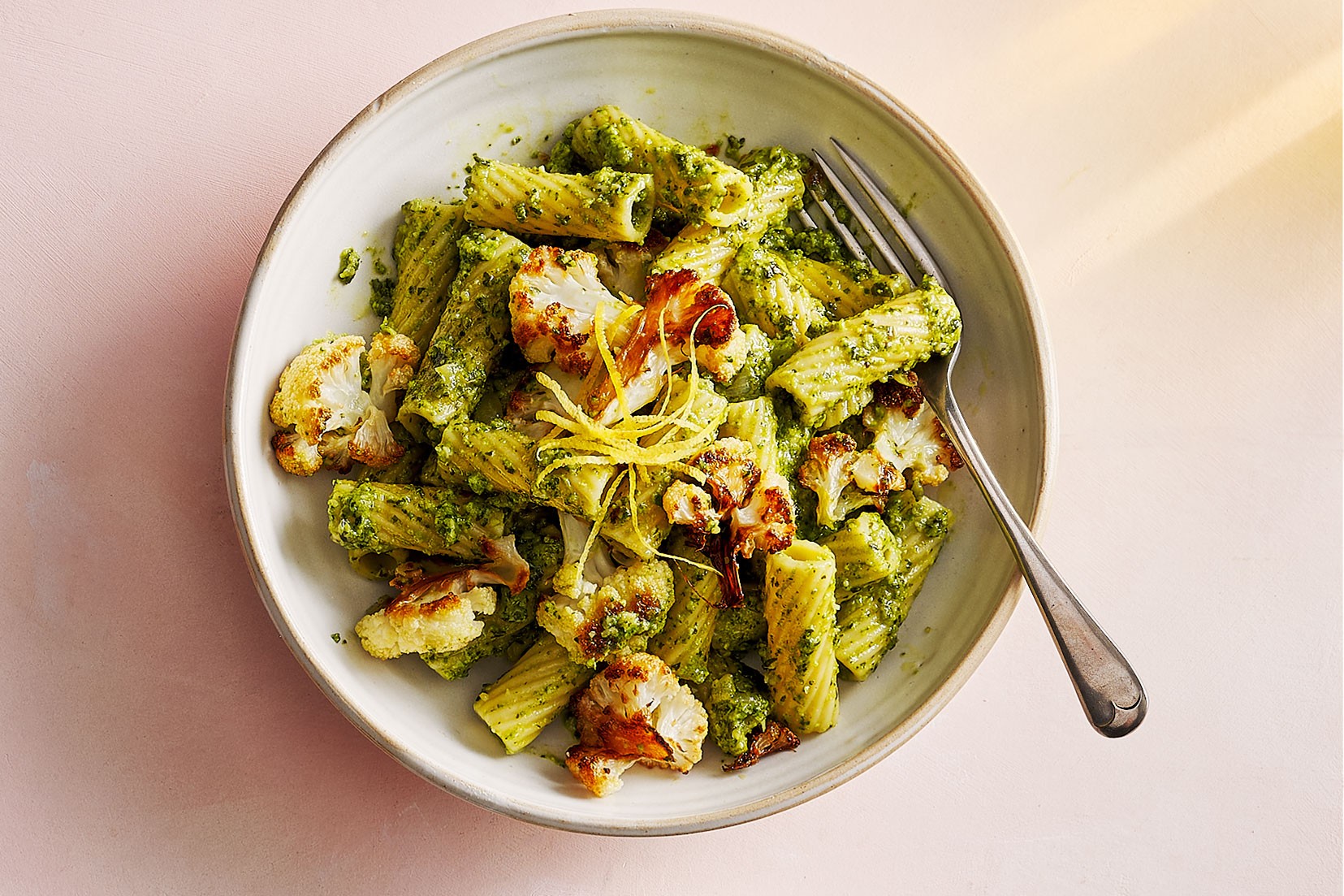 Bowl of pasta pesto topped with charred cauliflower and lemon zest