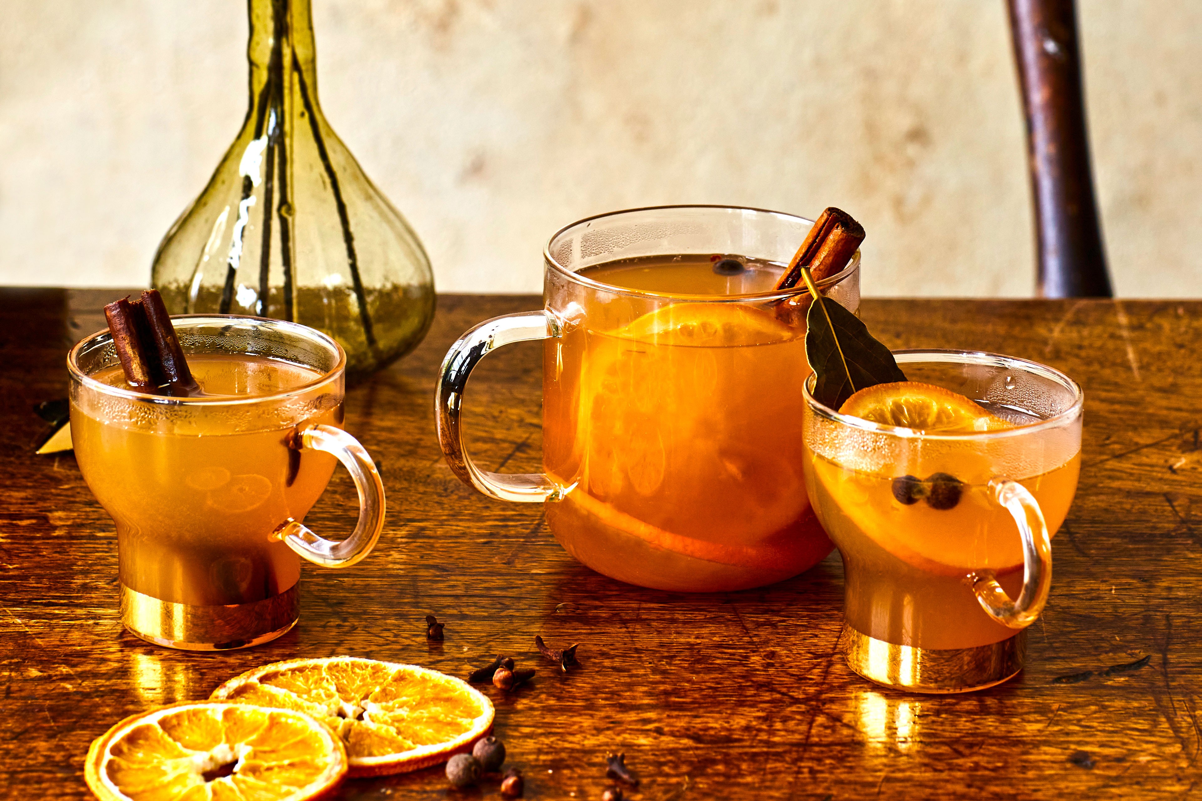 Three glass mugs of mulled cider with orange wheels inside