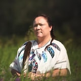 Brandy Callihoo stands in the middle of a field, holding a feather in her hands.