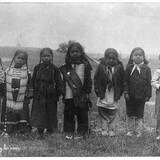 Seven small children stand in the grass. 