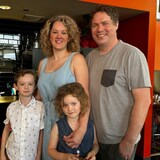 A family of four pose in their kitchen.