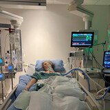 A woman on a ventilator, surrounded by machines, lies in a hospital bed.