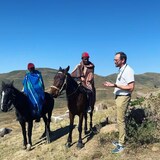 Two men on horseback speak to another man standing next to them.