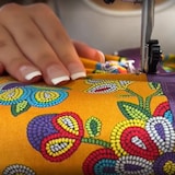 Two hands guiding the fabric of a ribbon skirt under a sewing machine.