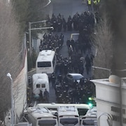 De nombreuses personnes en uniforme sortent de véhicules pour se diriger vers la résidence.