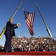 Donald Trump monte sur scène lors d'un rassemblement de campagne et pointe vers un drapeau géant des États-Unis. 