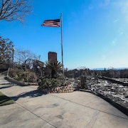 Un drapeau américain flotte au-dessus des restes carbonisés d'une maison brûlée dans le quartier de Pacific Palisades à Los Angeles, le 14 janvier 2025.