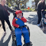 Un garçon en chaise roulante déguisé en Mario passe l'Halloween durant le jour.