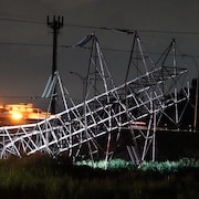 Un pylône électrique affaissé sur la pelouse en pleine nuit.