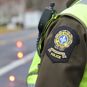 Une personne porte un uniforme de la Sûreté du Québec devant des fusées routières sur une route.