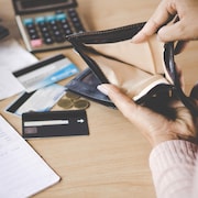 Une femme montre son porte feuille vide devant des cartes et de l'argent sur une table.