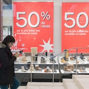 Une femme marchant dans la rue devant une vitrine affichant 50% de rabais