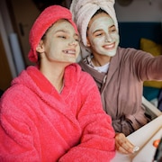 Deux jeunes adolescentes souriantes qui portent des masques de beauté se filment avec un téléphone mobile.