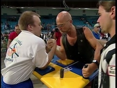 Deux athlètes s'affrontent lors d'une compétition de tir au poignet sous les yeux attentifs d'un arbitre. 