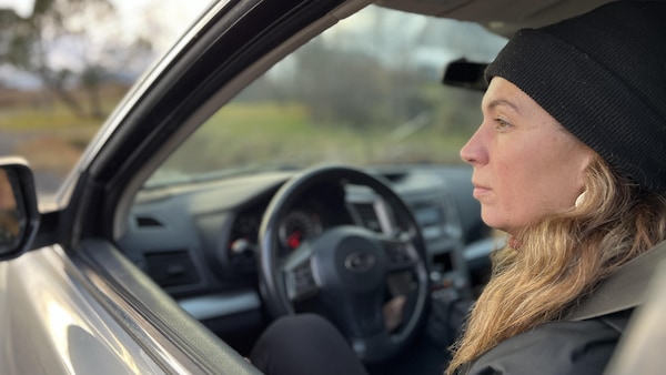 Une femme est assise au volant de sa voiture arrêtée et regarde au loin par la fenêtre.