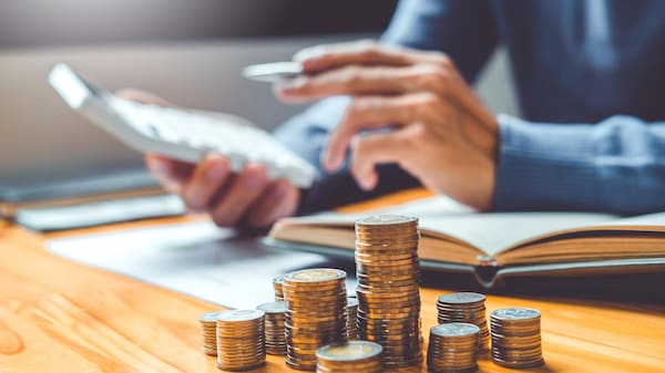 Une personne fait ses comptes, assise à une table, avec de nombreuses pièces de monnaie au premier plan.